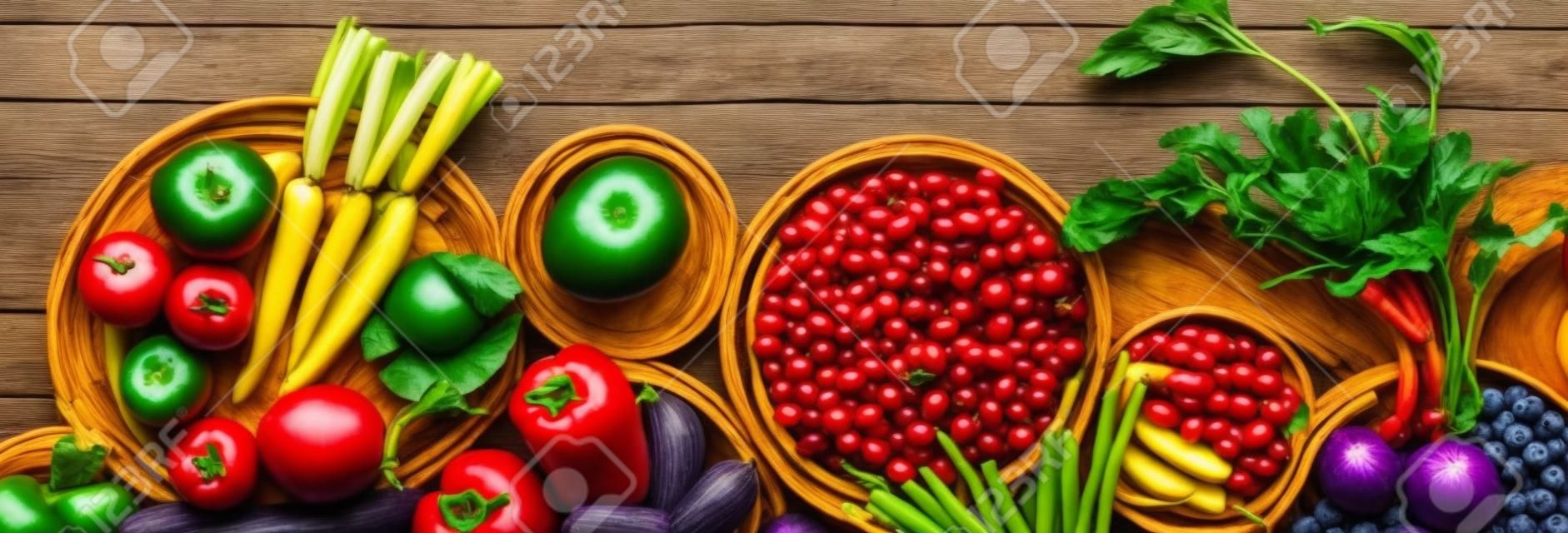 Narrow view of fresh fruits and vegetables in rainbow colours against a dark wooden background.