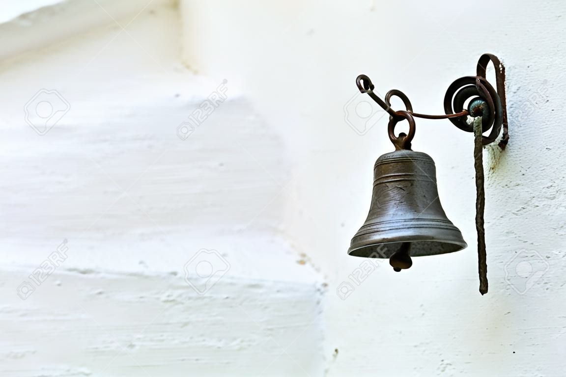 Closeup of an old small bell made of bronze hanging on a white wall