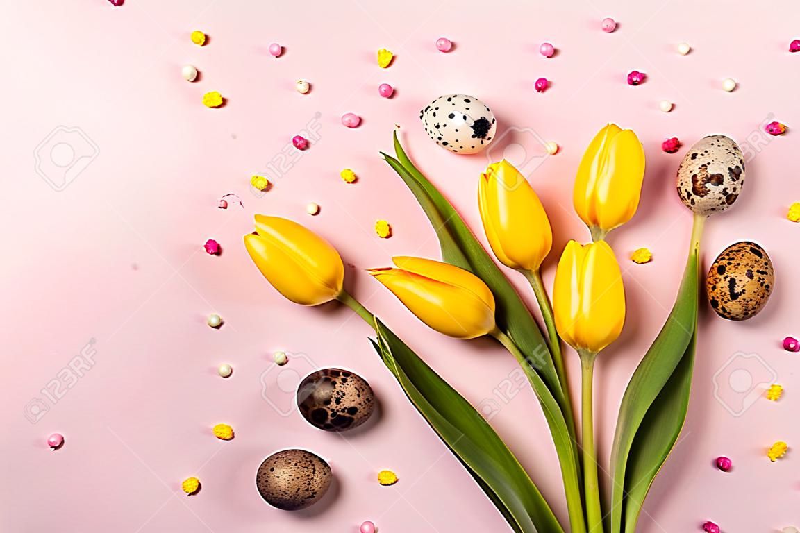 Yellow tulip flowers and quail eggs on pastel pink background.