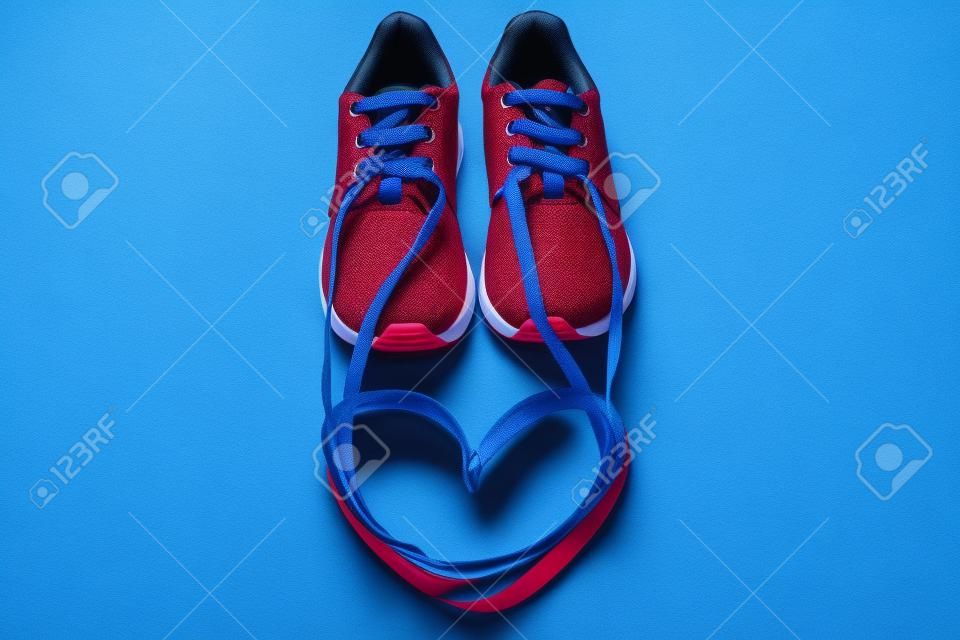 Red athletic sneakers and a heart symbol made of shoelaces on a blue background. Running passion romantic concept.