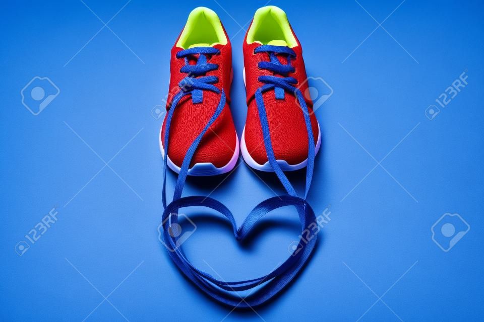 赤いアスレチックスニーカーと青い背景に靴ひもで作られたハートのシンボル。情熱的なロマンチックなコンセプトを実行します。