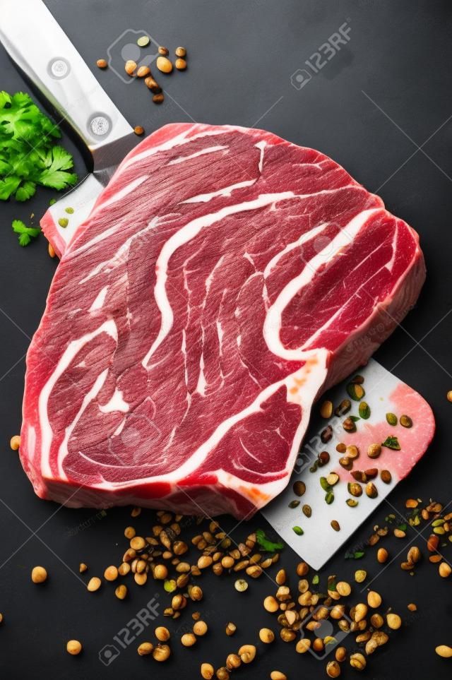 Fresh raw beef marbled steak. Chuck eye roll on a cleaver. Black background. Top view.