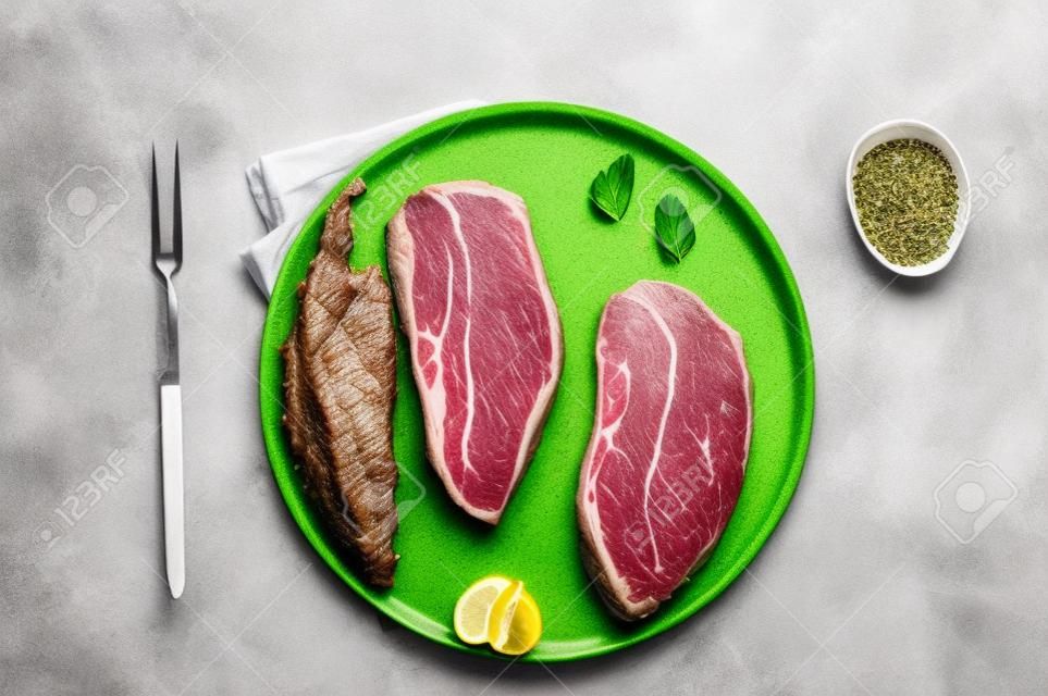 Raw Oyster Top Blade or flat iron roast beef meat steaks on a plate with herbs. White background. Top View