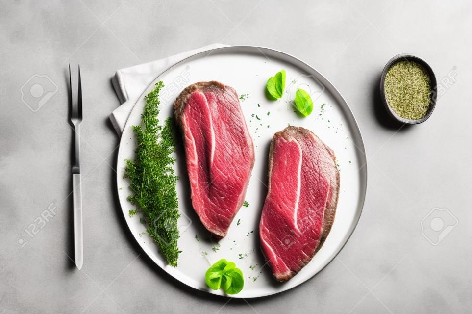 Raw Oyster Top Blade or flat iron roast beef meat steaks on a plate with herbs. White background. Top View