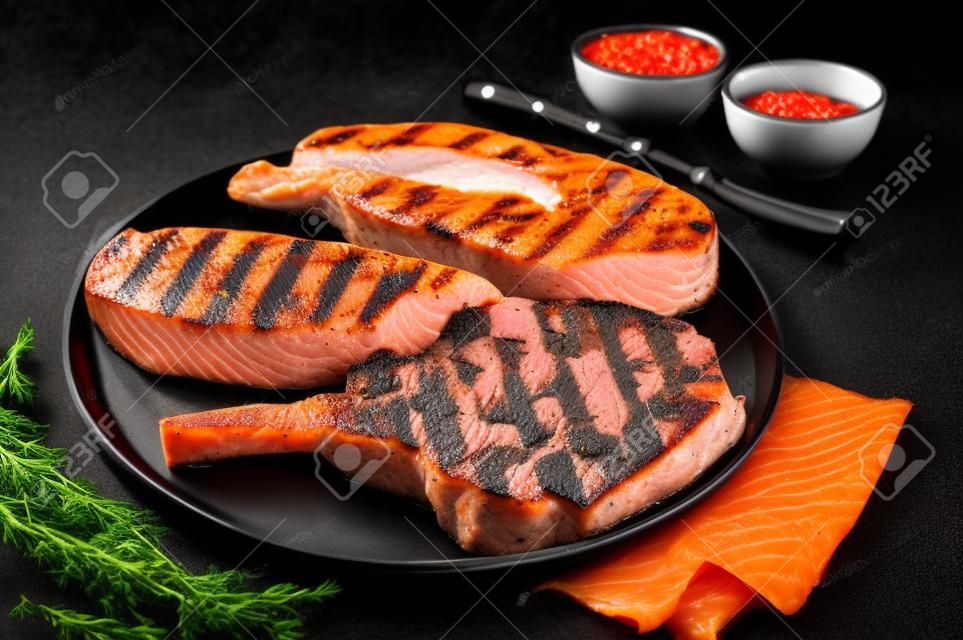 Bistecche di carne alla griglia - salmone di pesce, vitello di manzo e filetto di tacchino. Sfondo nero. Vista dall'alto