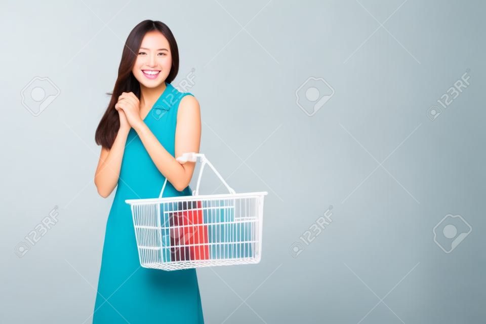 Mooie Aziatische vrouw glimlachen en houden winkelmand geïsoleerd op witte achtergrond