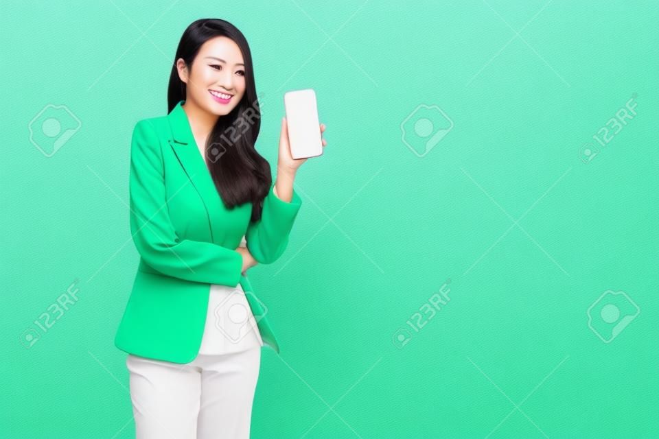 Retrato da mulher de negócios asiática que mostra ou que apresenta a aplicação do smartphone ou do telefone móvel isolada sobre o fundo verde, modelo tailandês asiático