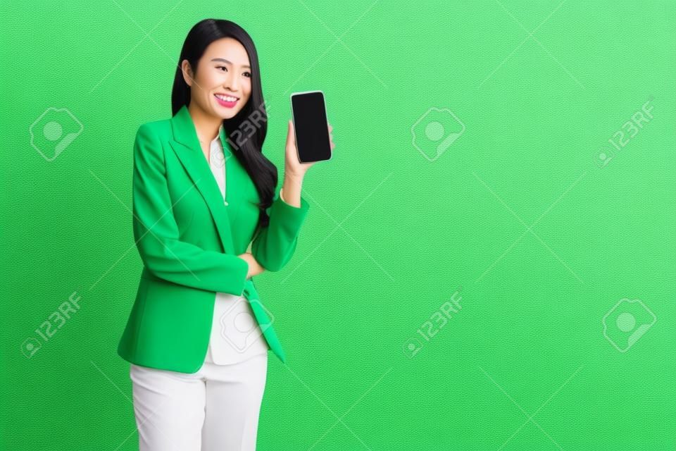 Ritratto di donna d'affari asiatica che mostra o presenta l'applicazione per smartphone o telefono cellulare isolata su sfondo verde, modello asiatico tailandese