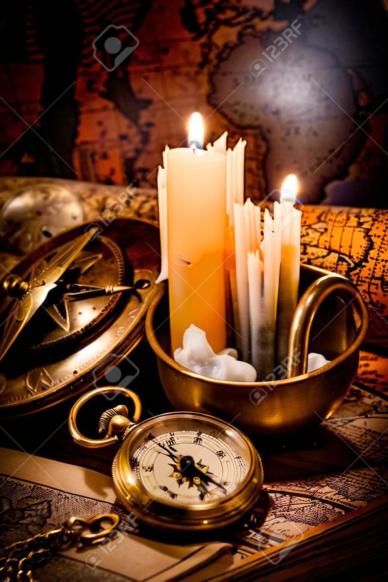 Vintage bussola, orologio da tasca si trovano su una vecchia mappa antica con una candela accesa