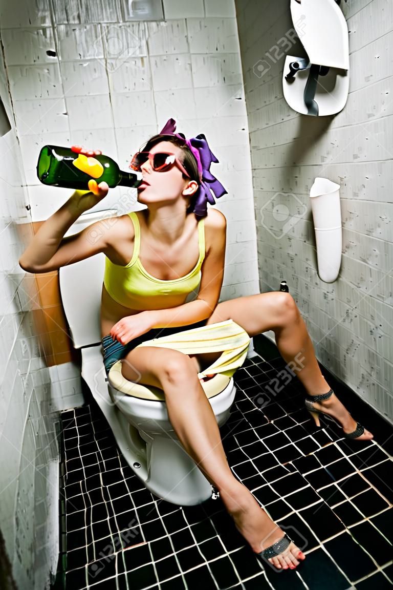 Девушка сидит в туалете с бутылкой алкоголя