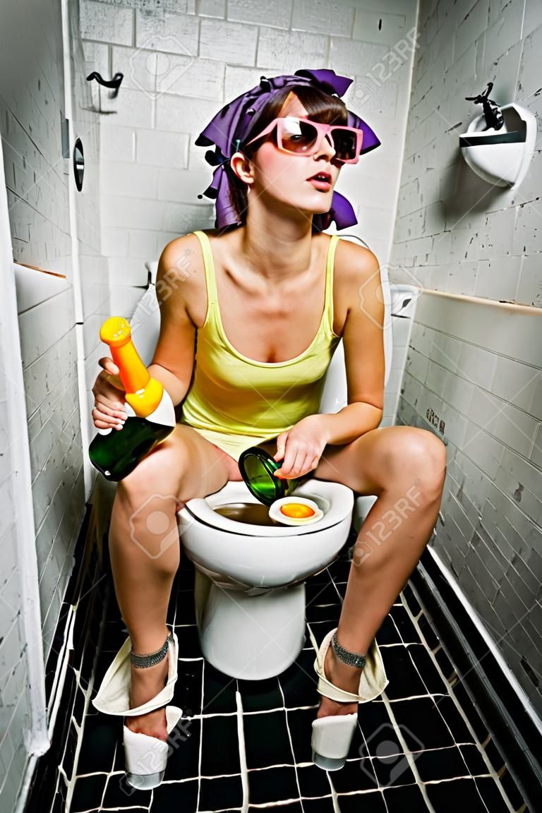 アルコールのボトルをトイレに座っている女の子