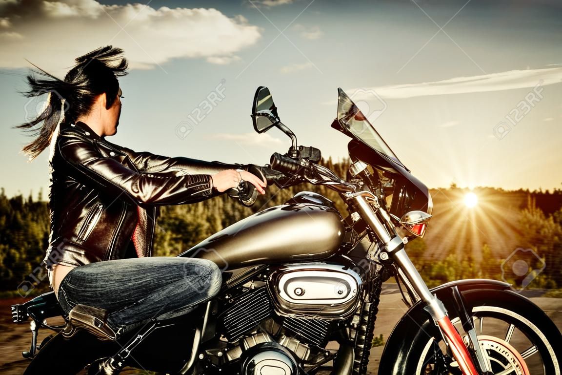 Bir motosiklet üzerinde bir deri ceket bisikletçinin kız günbatımı bakarak