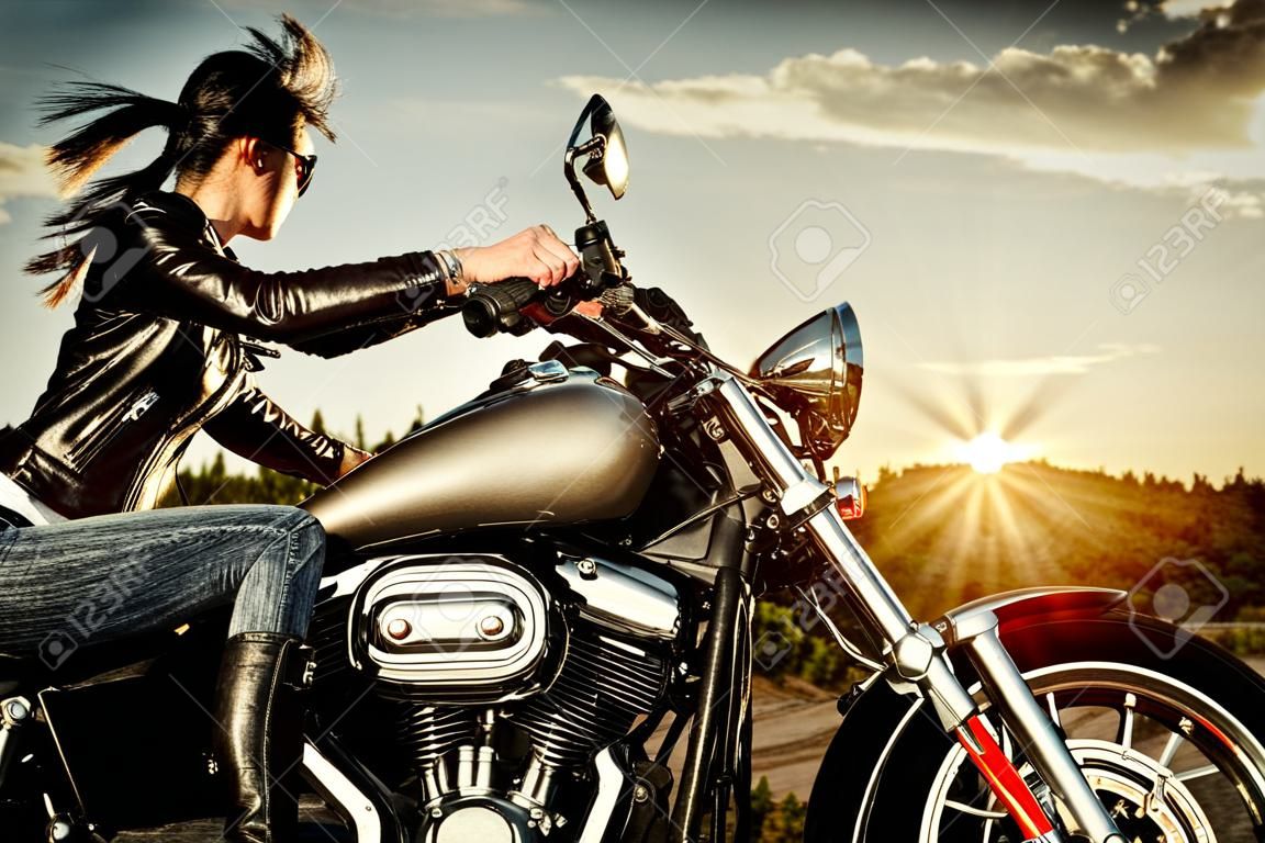 Biker girl in a leather jacket on a motorcycle looking at the sunset 