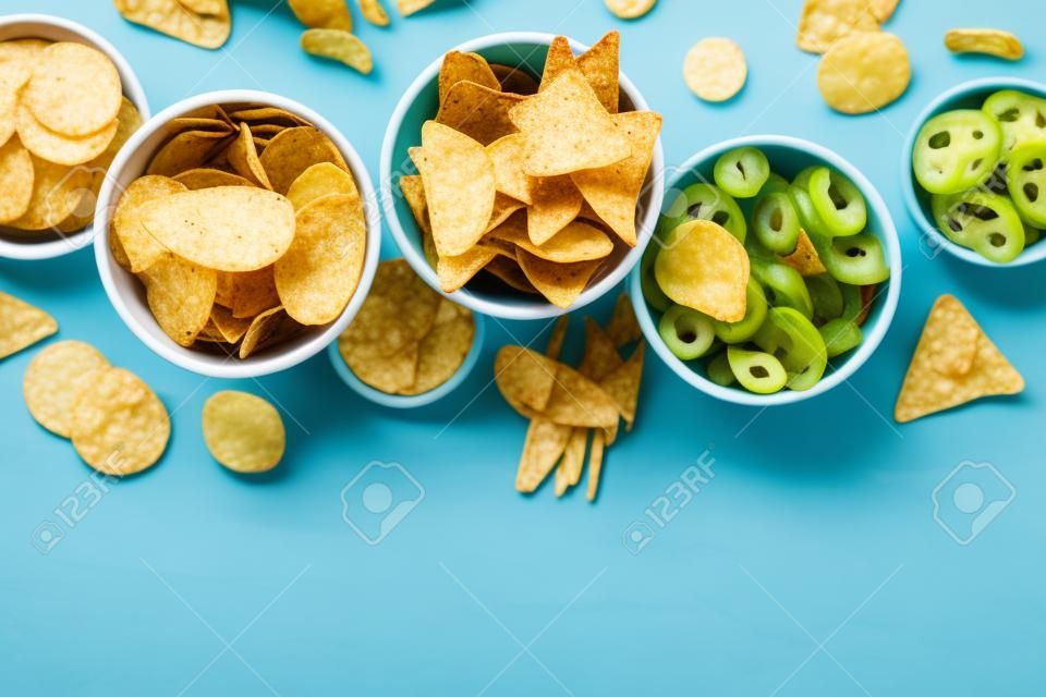 Patatas fritas y tortillas y otros bocadillos salados, tomados desde arriba con espacio para copiar. comida de fiesta sobre un fondo azul verde azulado. una mezcla de aperitivos en tazones