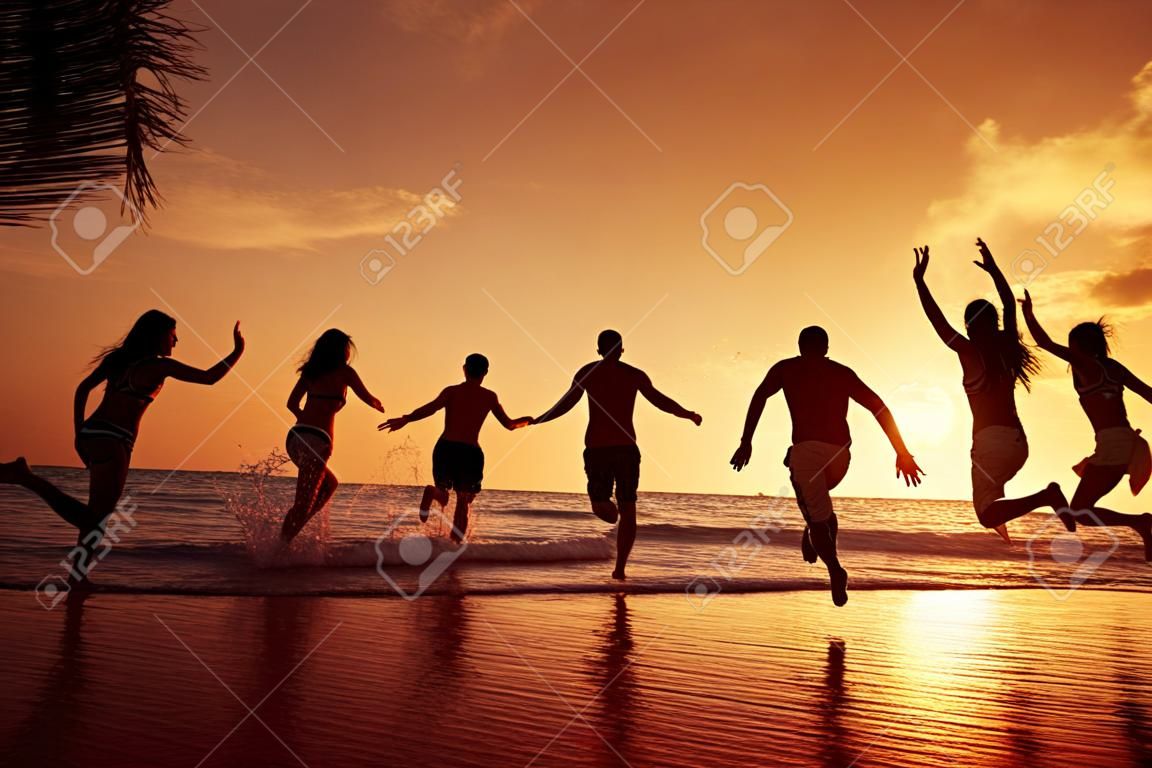 Grupo de jovens felizes está correndo no fundo da praia do por do sol e do mar. Província de Krabi, Tailândia