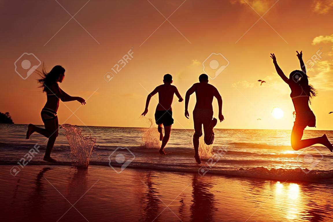 Grupo de jovens felizes está correndo no fundo da praia do por do sol e do mar. Província de Krabi, Tailândia
