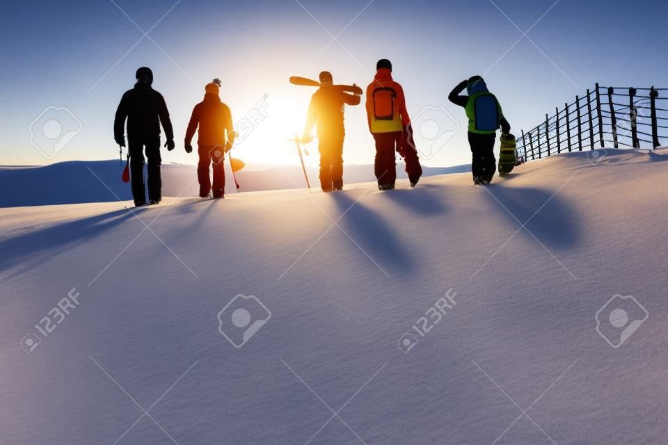 Friends with ski and snowboards walking to sunset