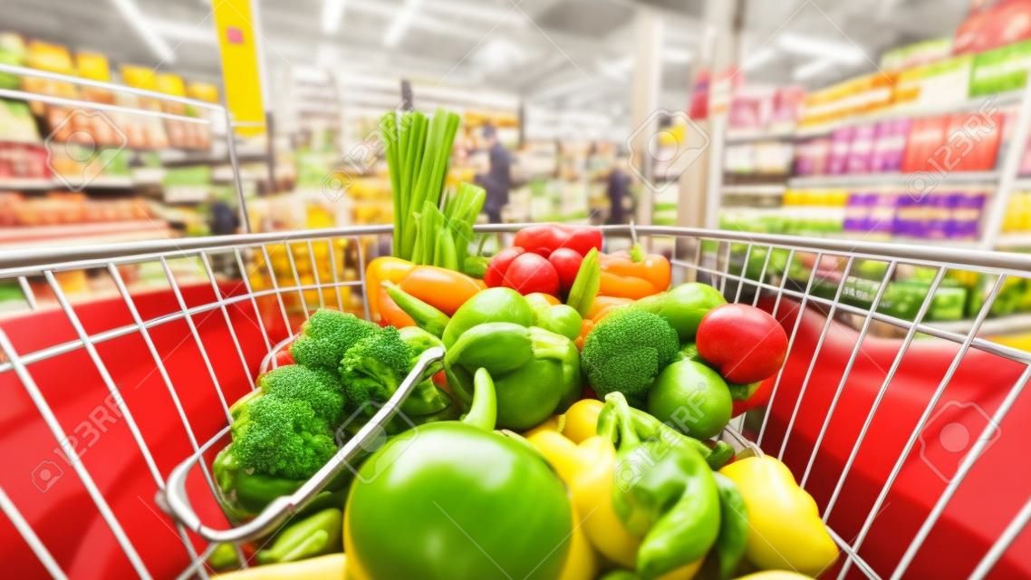 Grocery shop cart in supermarket filled up with fresh and healthy food products as seen from the customers point of view with people shopping in background