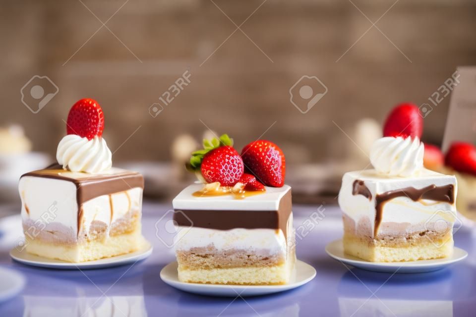 Selection of desserts: amandine, meringue with chocolate and strawberries, caramel cake, in a restaurant setting, blurred background