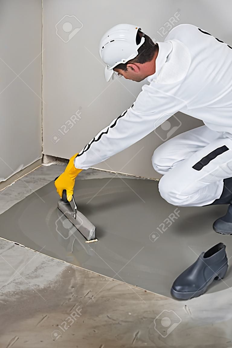 Worker spreading self leveling compound with trowel
