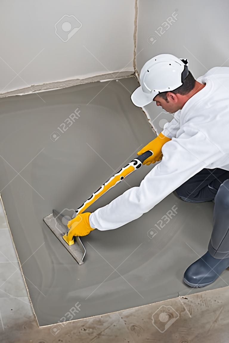 Worker spreading self leveling compound with trowel