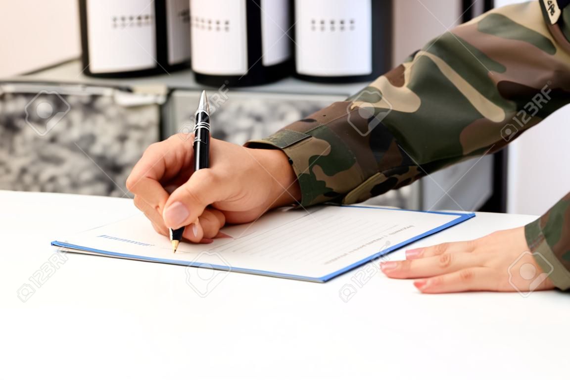 Primo piano di una mano di un militare che scrive o firma un documento su una scrivania nell'accademia militare