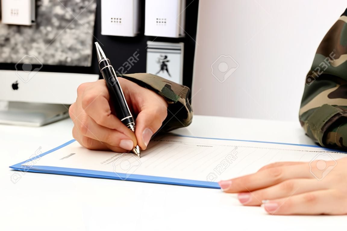 Primo piano di una mano di un militare che scrive o firma un documento su una scrivania nell'accademia militare