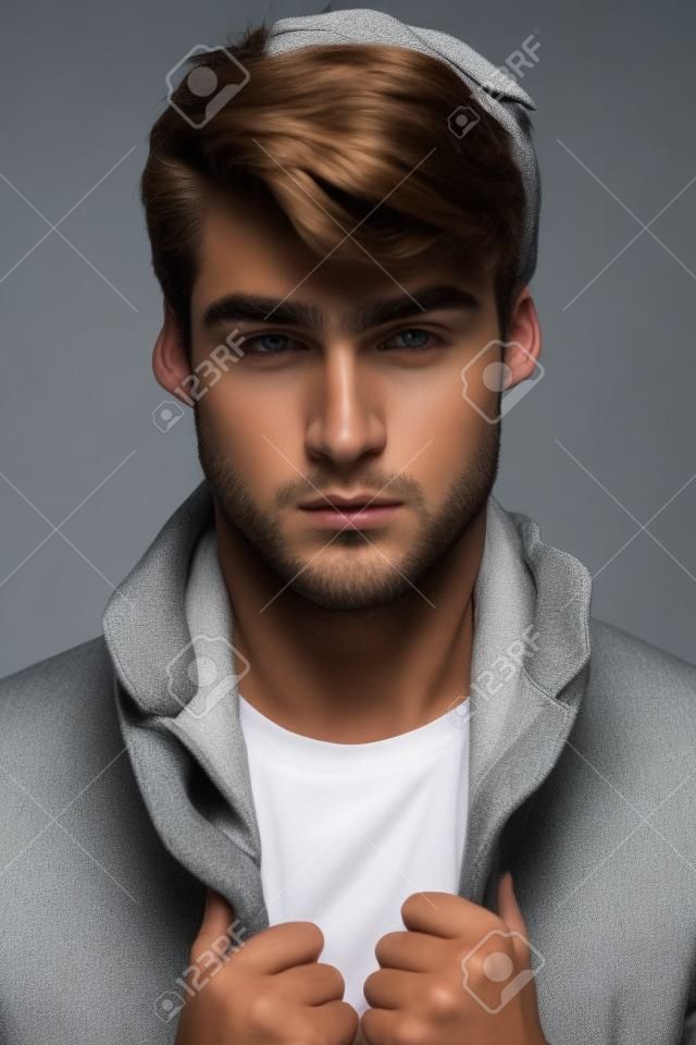Portret van een jong mannelijk model met mooi gezicht en handen op zijn jas