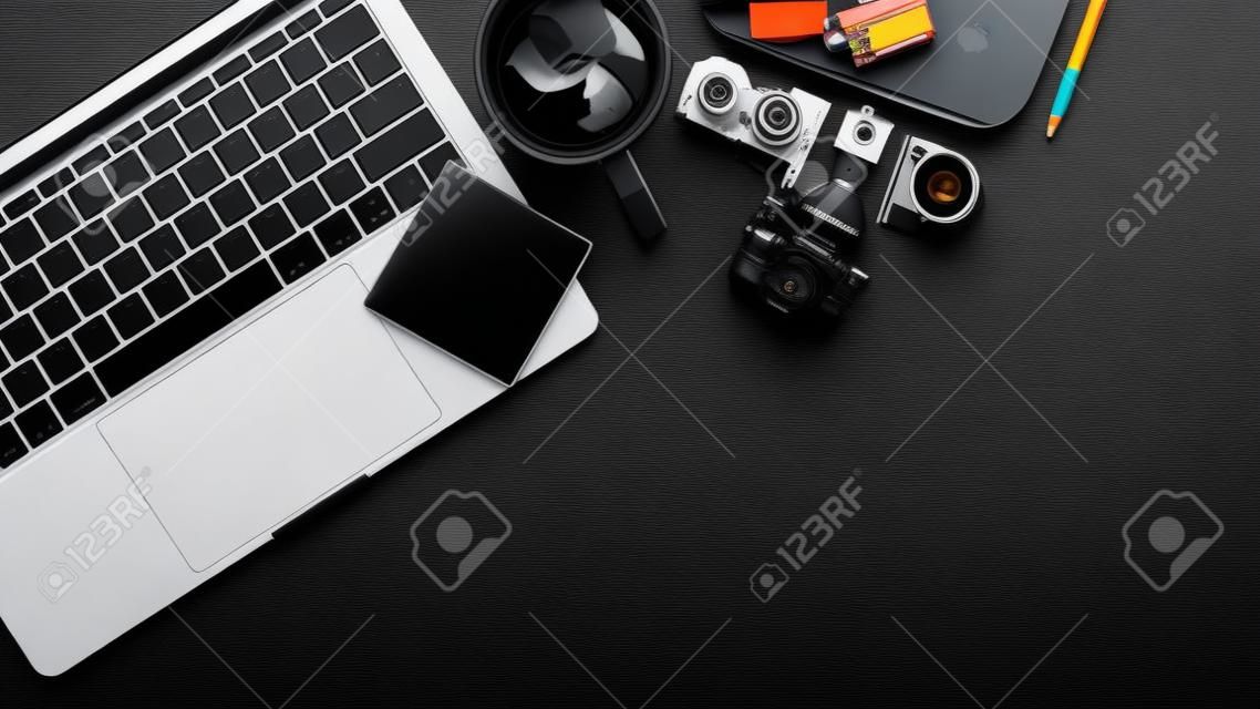 Vue de dessus de l'espace de travail avec ordinateur portable, appareil photo, fournitures et espace de copie sur un bureau noir