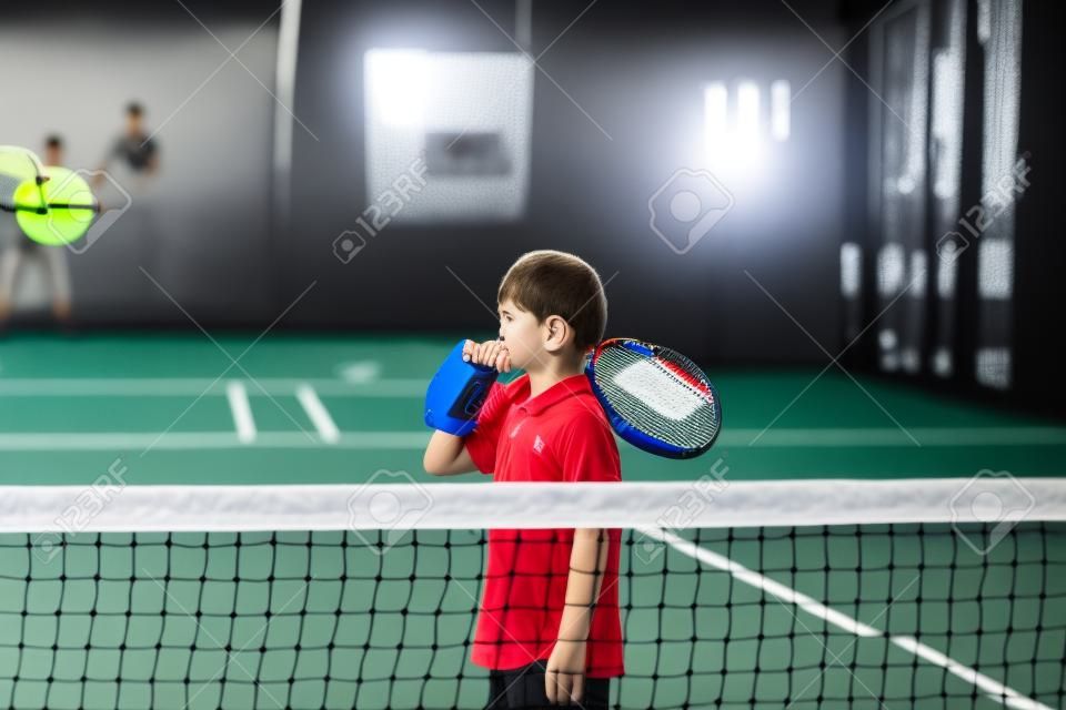 Monitoruj nauczanie dziecka klasy Padel, jego uczeń - trener uczy małego chłopca, jak grać w Padla na krytym korcie tenisowym