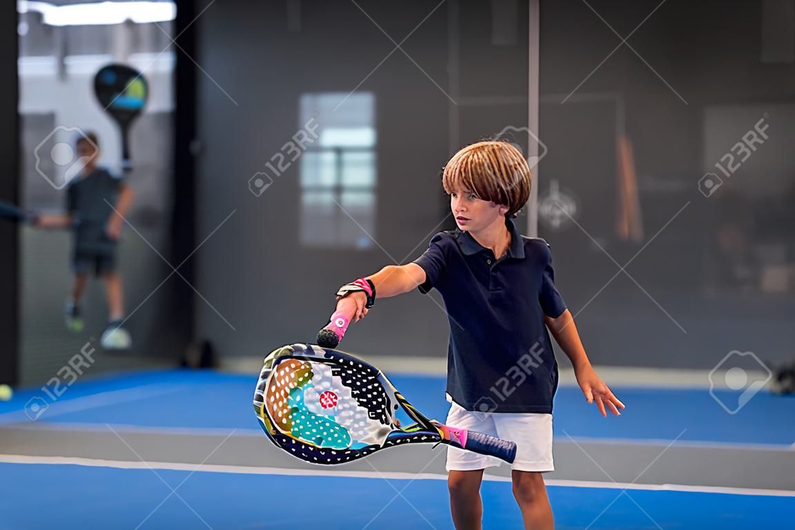 Monitor unterrichtet Kind, seinen Schüler, im Padel-Unterricht - Trainer bringt kleinem Jungen bei, wie man Padel auf einem Indoor-Tennisplatz spielt