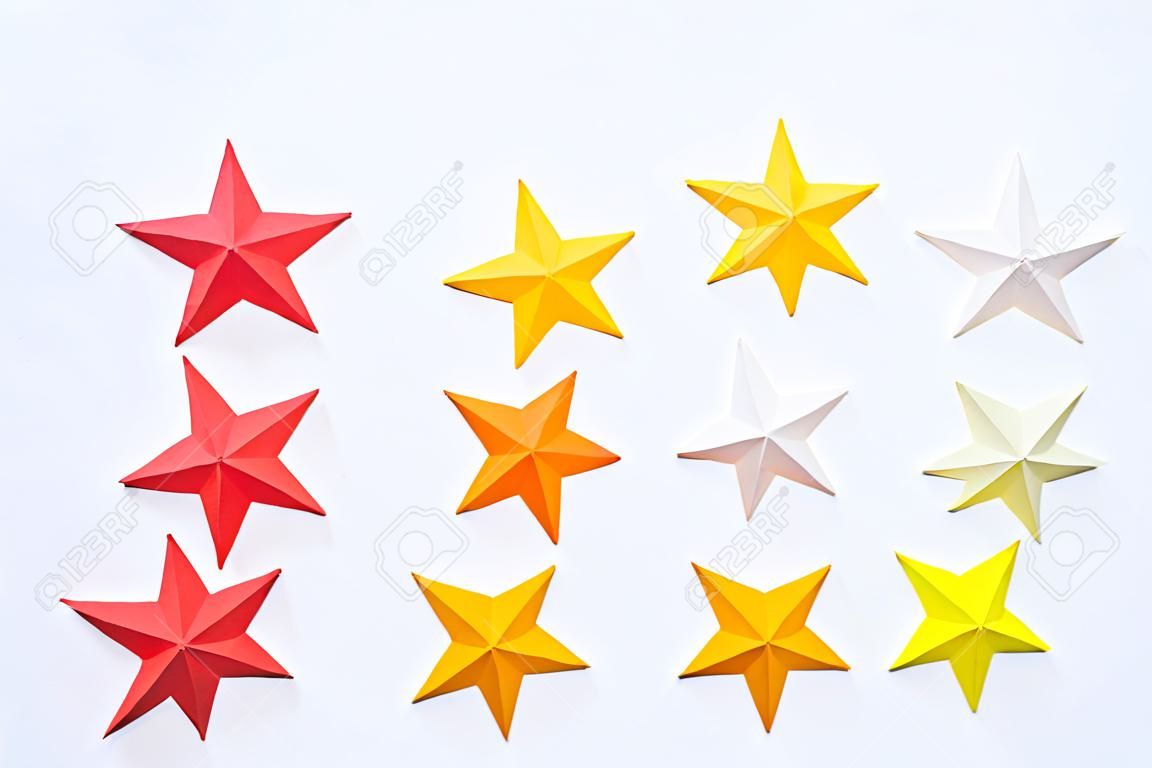 Una estrella hecha de papel del color rojo anaranjado amarillo. Cielo estrellado de decoración festiva. Fondo blanco. Pasatiempo favorito. Creatividad con niños.