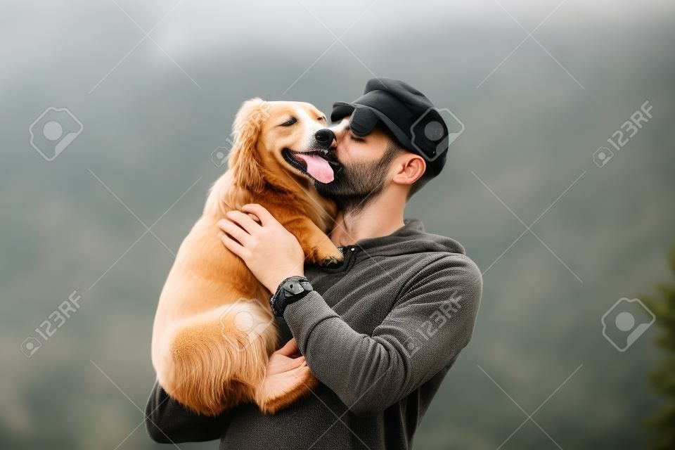 Homem segurando o cão em seus braços e beijando-o ao ar livre. Cão e proprietário juntos. Amor para animais de estimação