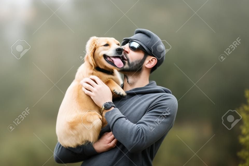 Homem segurando o cão em seus braços e beijando-o ao ar livre. Cão e proprietário juntos. Amor para animais de estimação
