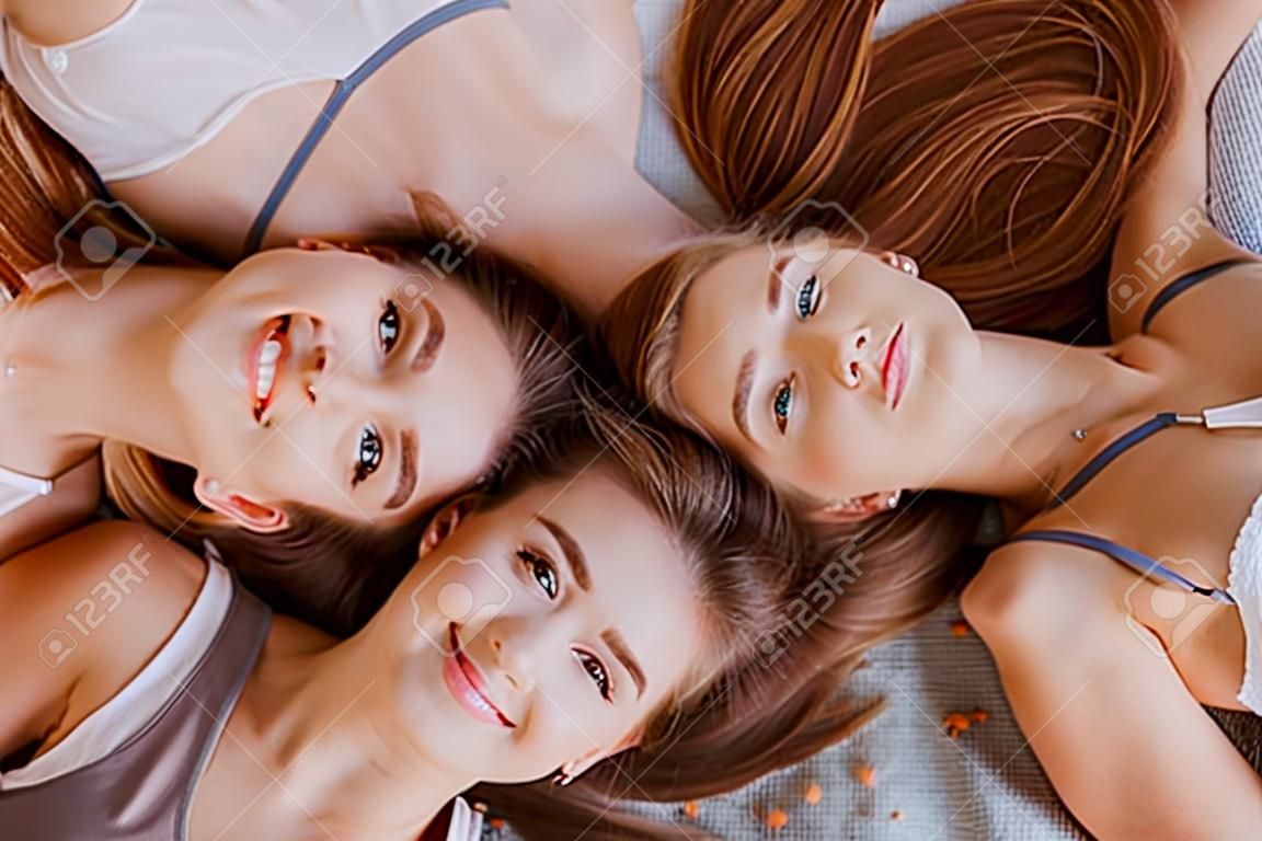 Women rest and have fun. Girlfriends laugh at home lying on the floor on pillows. Tree girls make homemade face and hair beauty masks. Women take care of youthful skin.