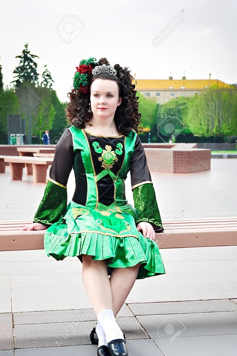 Young woman in irish dance dress and wig sitting on the bench outdoor