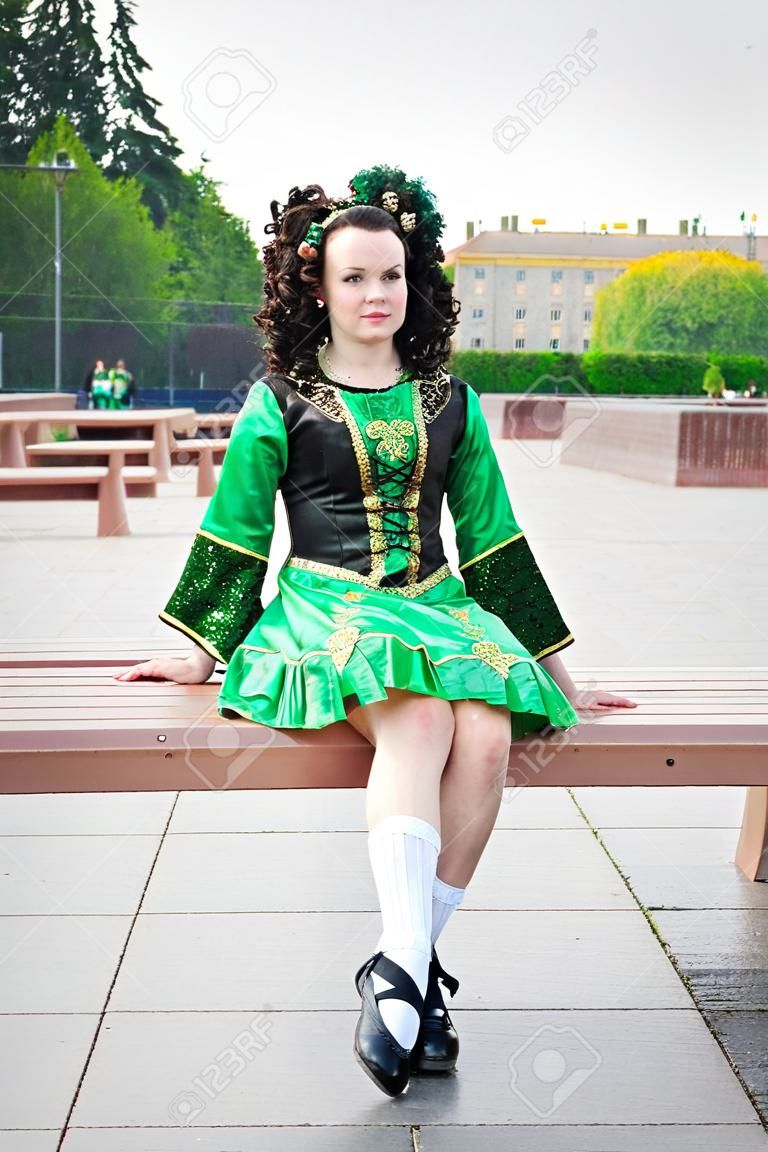 Young woman in irish dance dress and wig sitting on the bench outdoor