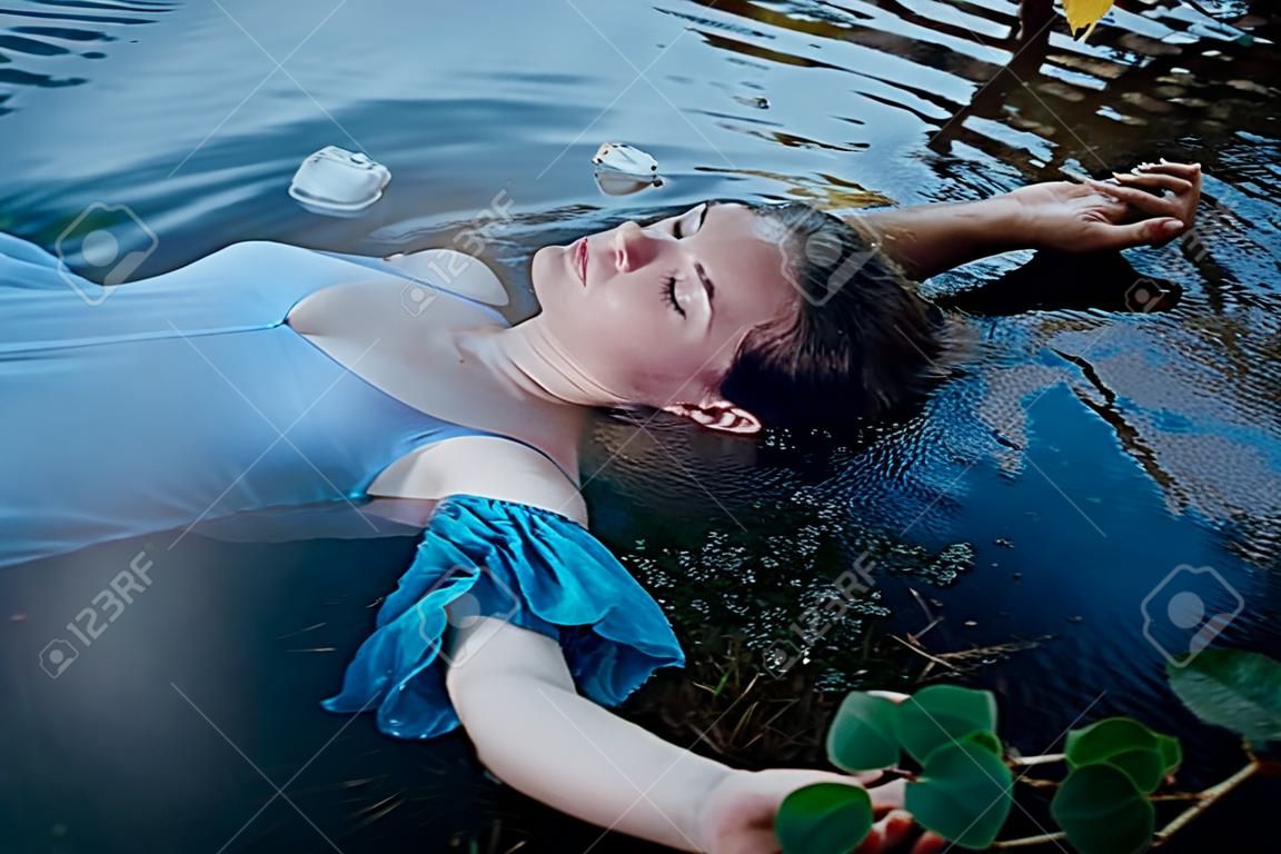 年轻漂亮的穿蓝色衣服的溺水妇女躺在户外的水里