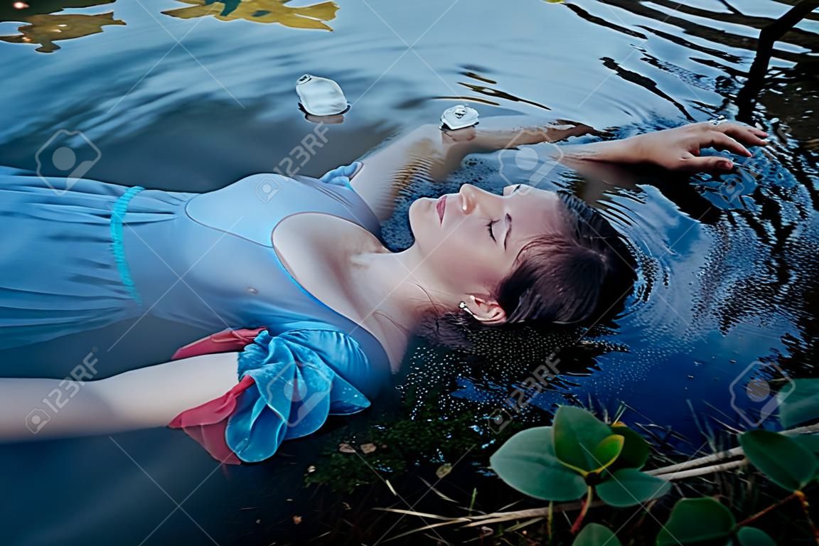年轻漂亮的穿蓝色衣服的溺水妇女躺在户外的水里