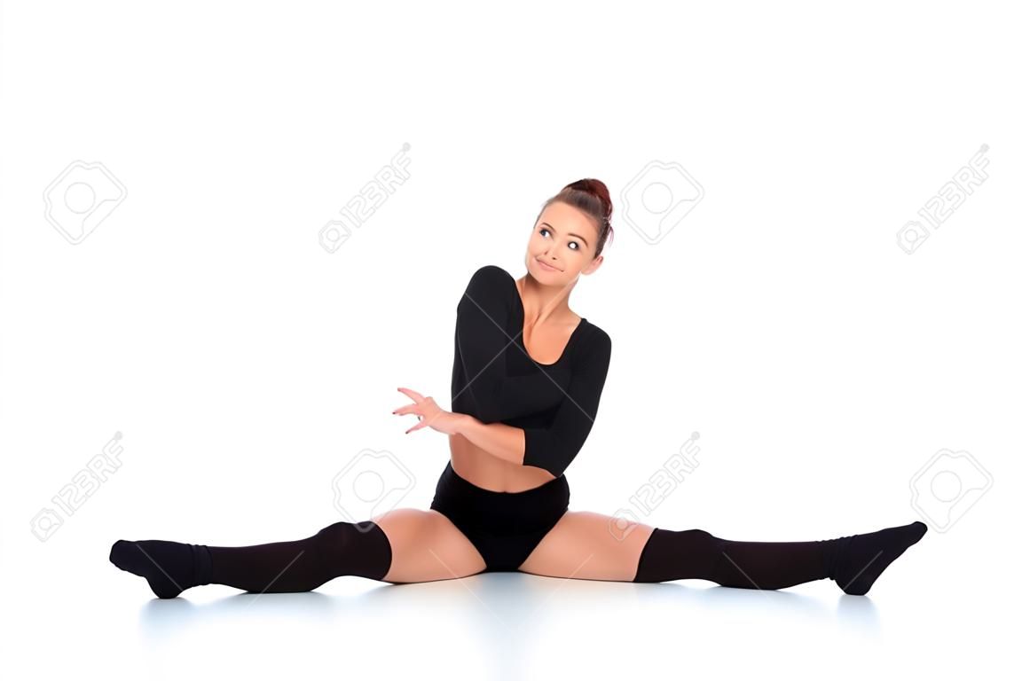 Supple young woman in a leotard and leggings doing the splits and smiling happily at the camera over a white background