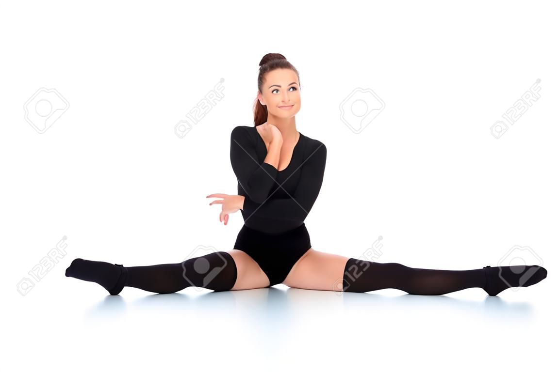 Supple young woman in a leotard and leggings doing the splits and smiling happily at the camera over a white background