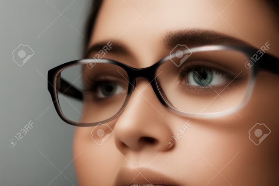 Zbliżenie młodej kobiety o brązowych oczach i okularach odwracającej wzrok na szarym tle