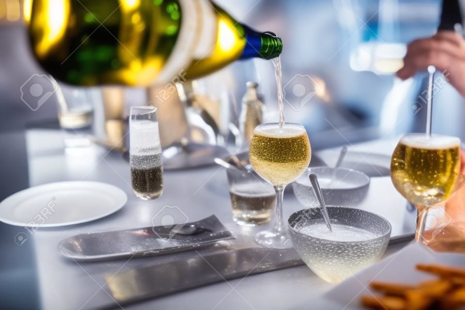 Ein Mann gießt ein Glas Champagner ein, Nahaufnahme fließender Sektgerichte, Snacks, Teller, Soßen, Menschen, die im Hintergrund speisen, ein freundliches Mittagessen oder eine Party in einem Café oder Restaurant