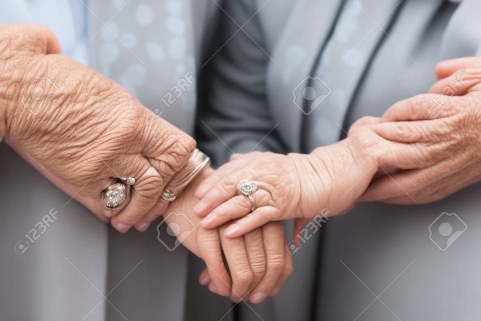 Close-up of aged hands. The female hand of a senior lady with rings on her fingers and a neat manicure covers the old male hand of her husband. Gentle handshakes of an elderly couple. Generated by A.I.