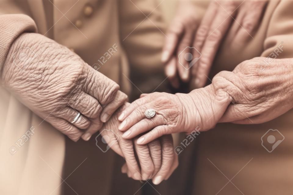 Close-up of aged hands. The female hand of a senior lady with rings on her fingers and a neat manicure covers the old male hand of her husband. Gentle handshakes of an elderly couple. Generated by A.I.
