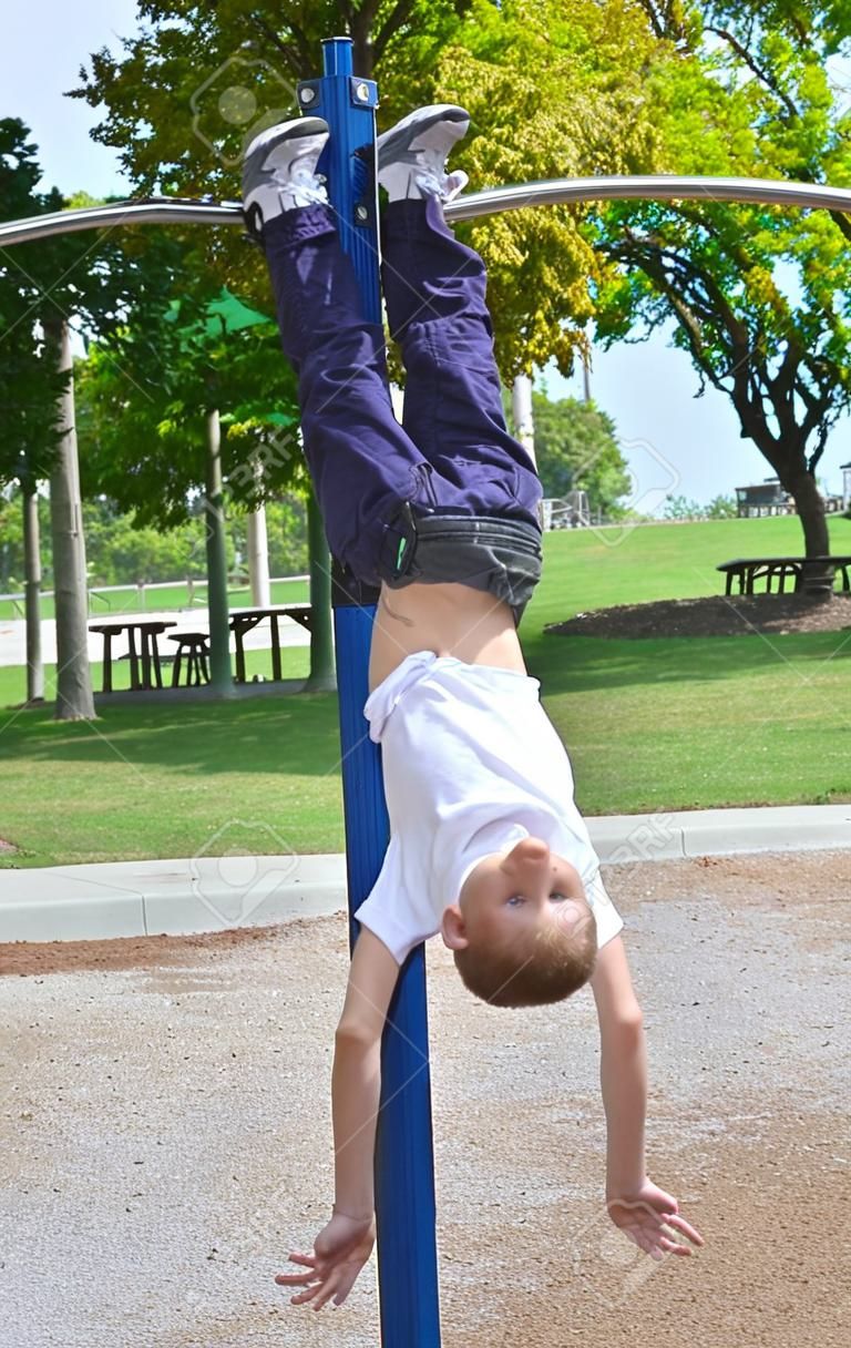 Preteen boy hanging upside down from high bar in park