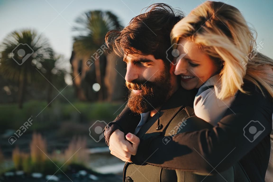 Blonde woman holding in her boyfriend back while they enjoy a date together at sunset.