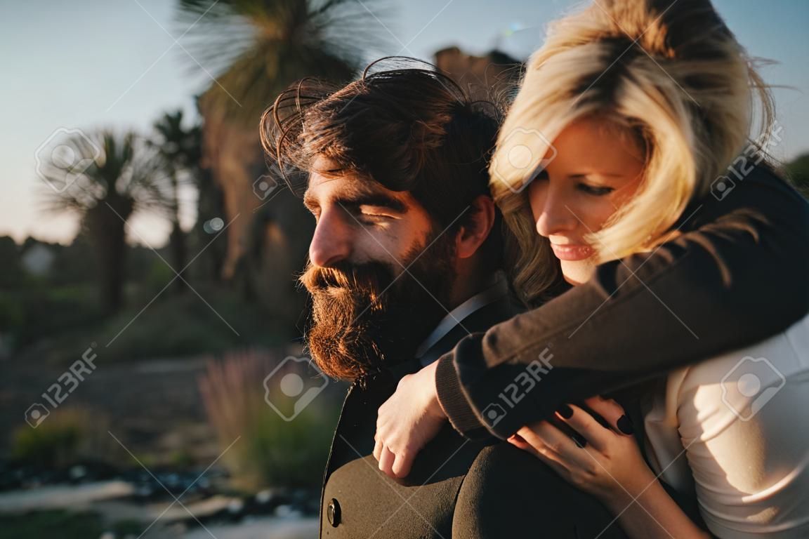 Blonde woman holding in her boyfriend back while they enjoy a date together at sunset.