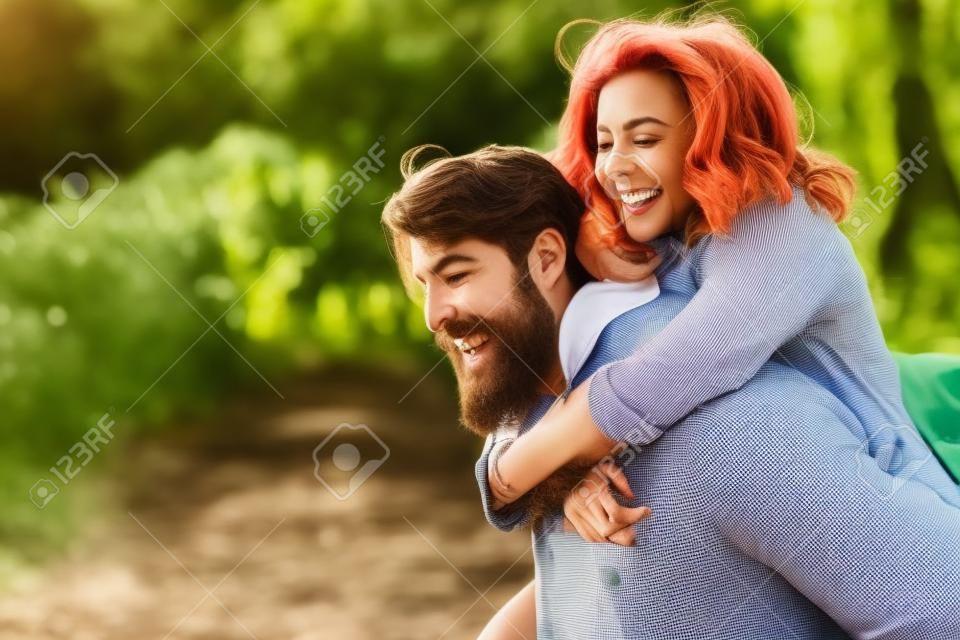 Cool indie couple having fun outdoors while he gives her a piggyback.