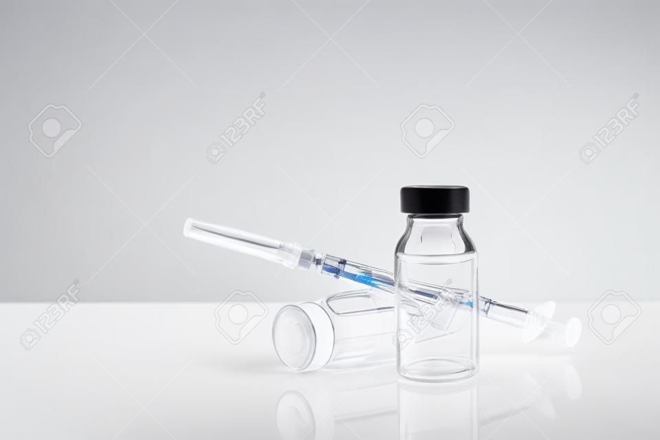 Buteleczki z lekarstwem i strzykawką na białym methacrylate stole z nadokiennym tłem. Poziomy skład. Przedni widok.